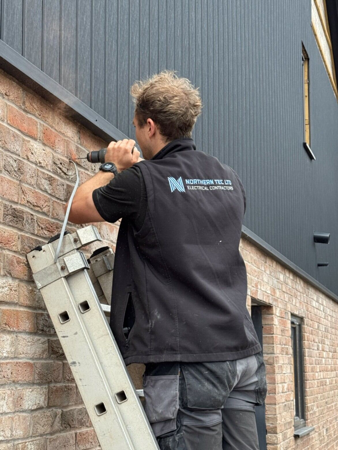Northern Tec engineer first-fixing electrical cable through composite decking on a rooftop terrace
