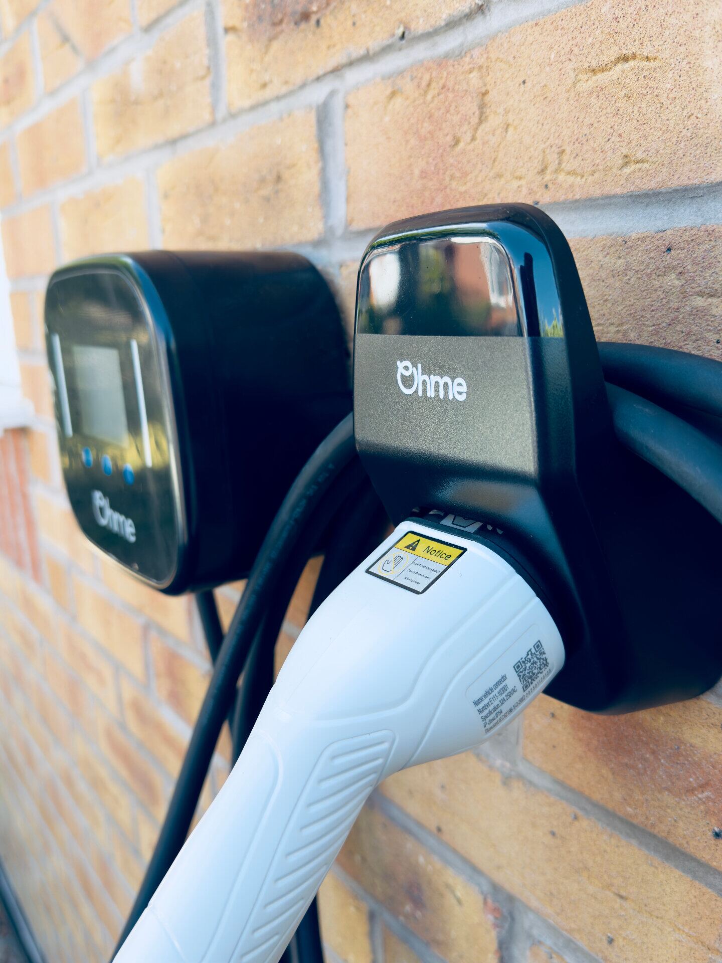 Close-up of an Ohme home EV charger plugged in and ready to charge on a brick wall