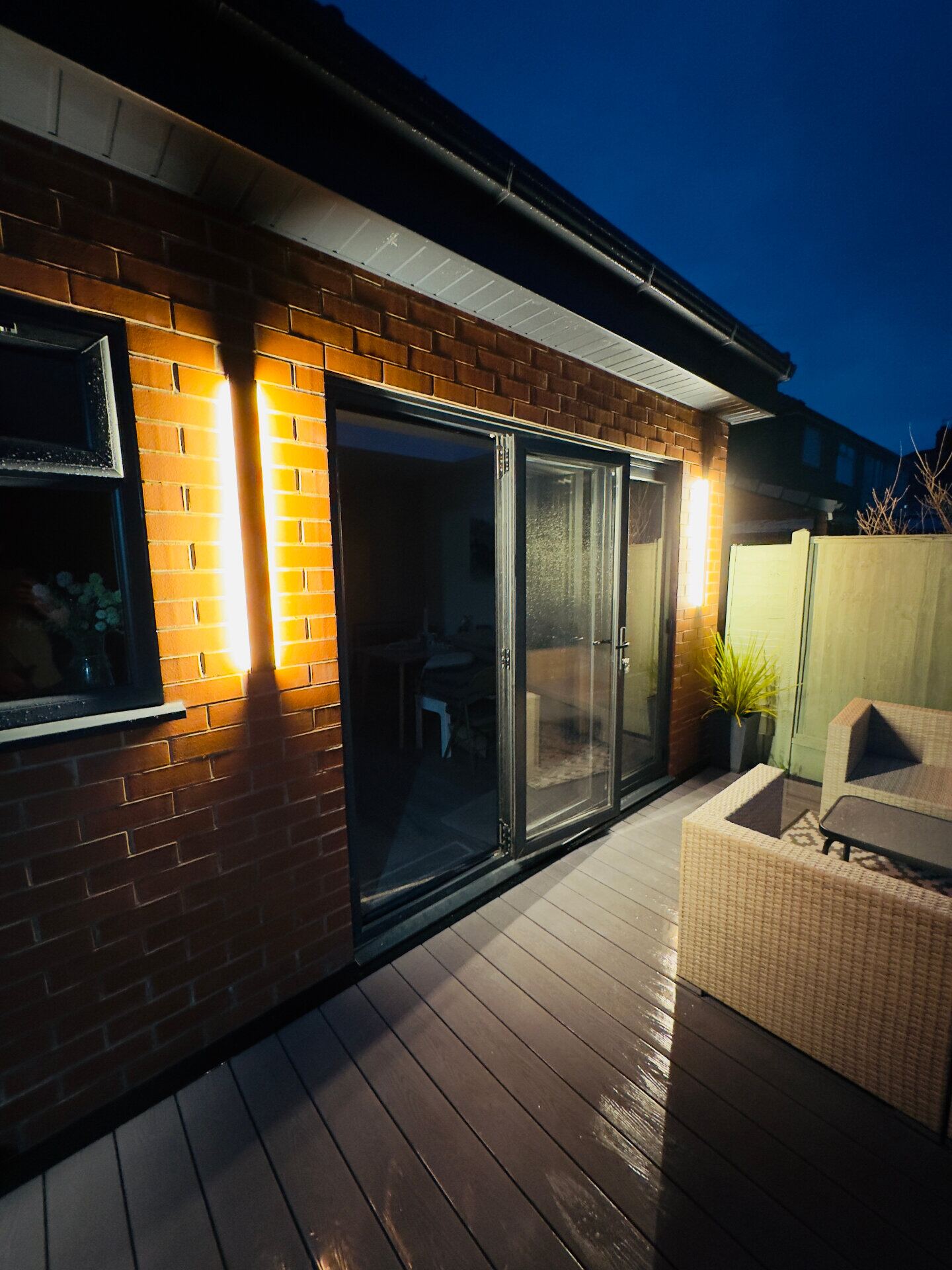 Exterior up-down wall lights illuminating a brick extension and patio at dusk